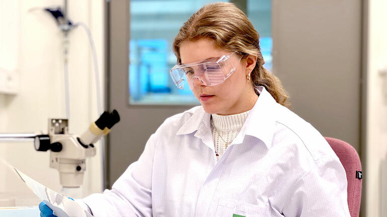Vanessa med hestehale og hvit frakk og beskyttelsesbriller jobber foran stetoskop i lab
