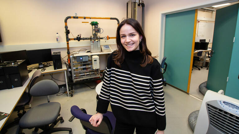 Thea stående i lab med stripete genser og mørkt, langt hår